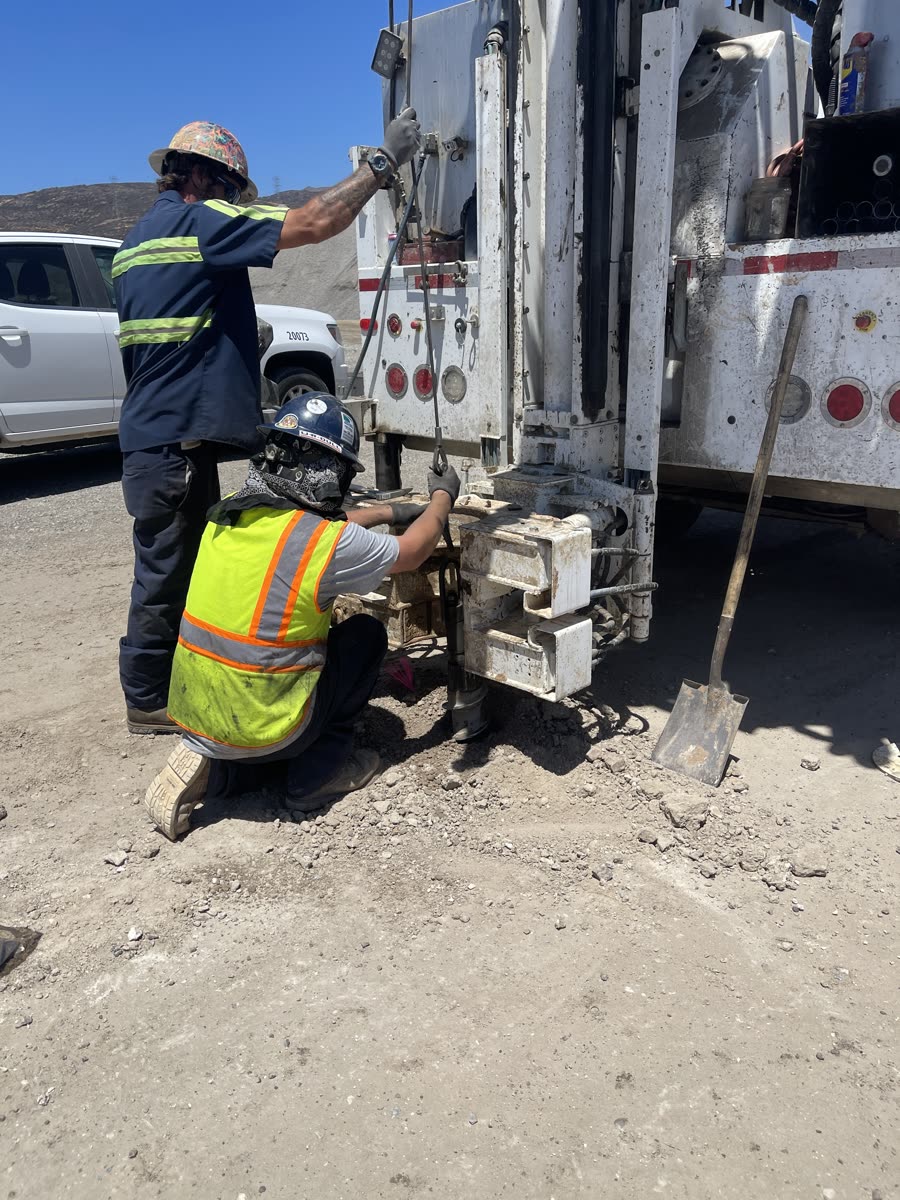 Two Pacific Drilling crew members in high-visibility gear working together at the back of a truck-mounted rig
