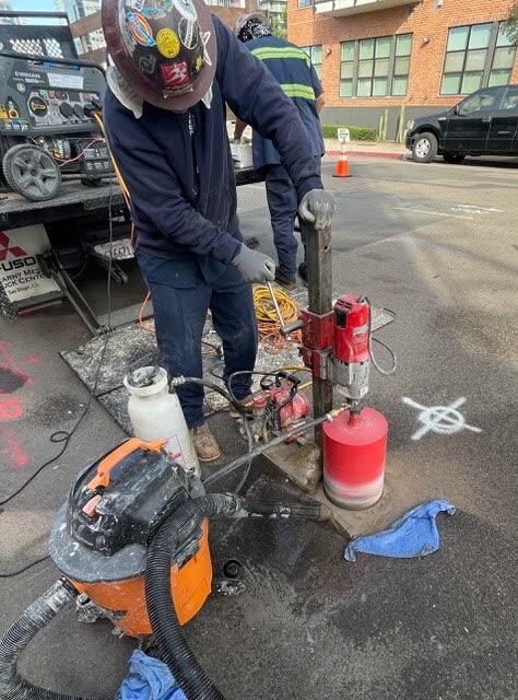 Two workers running a core drill through asphalt pavement.